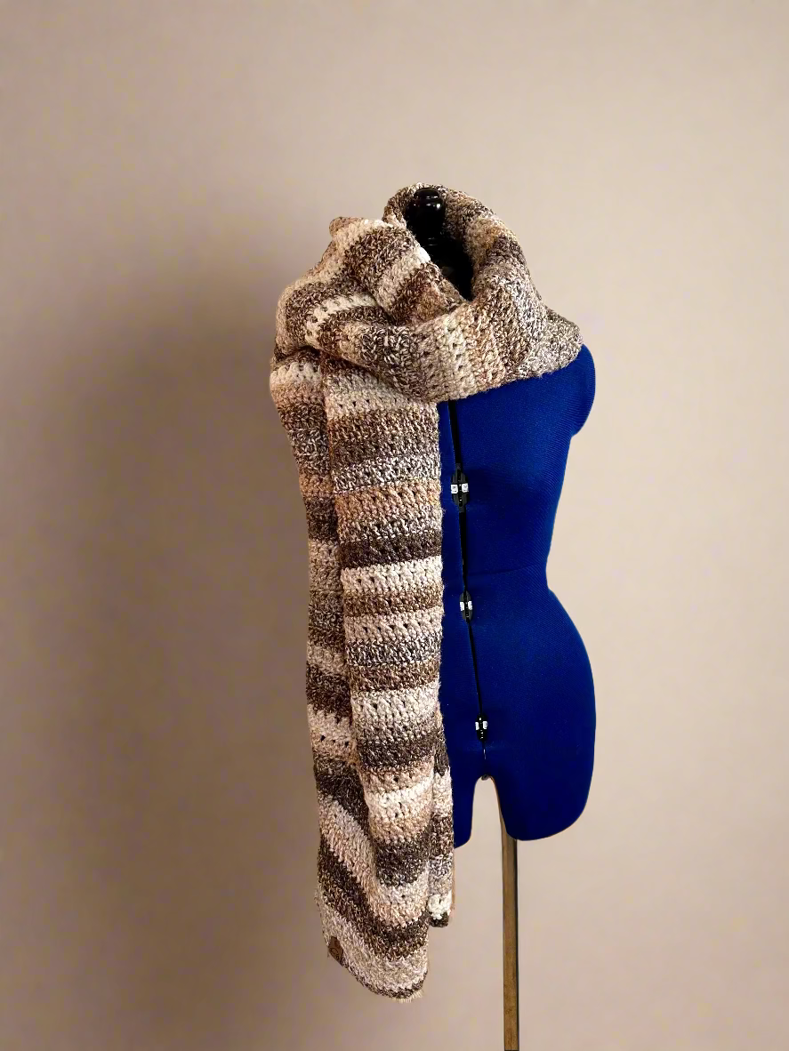 Knitted scarf draped over a blue mannequin against a wall with yarn and knitting supplies.