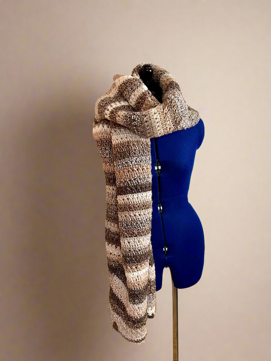 Knitted scarf draped over a blue mannequin against a wall with yarn and knitting supplies.